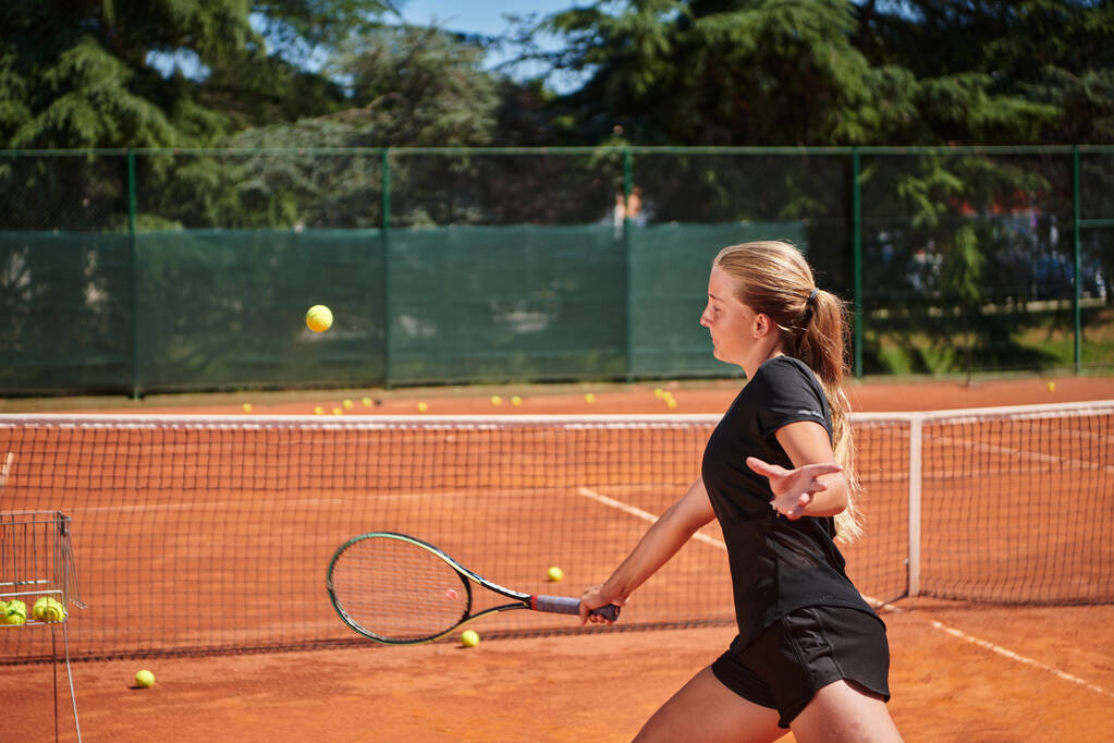 Nuori tyttö osoittaa tennistaitoja kilpailukykyisessä ottelussa aurinkoisena päivänä tenniskentän modernin estetiikan ympäröimänä. - Valokuva, kuva