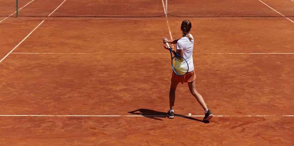 Una giovane ragazza che dimostra abilità nel tennis in una partita competitiva in una giornata di sole, circondata dall'estetica moderna di un campo da tennis - Foto, immagini