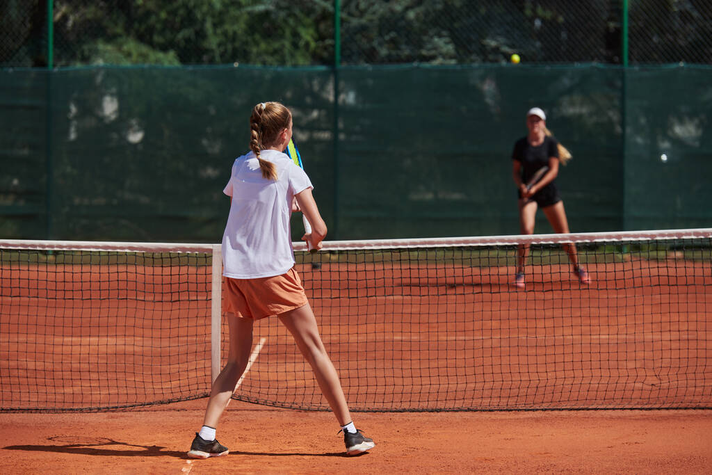 Молоді дівчата в жвавому тенісному матчі в сонячний день, демонструючи свої навички та ентузіазм на сучасному тенісному корті
 - Фото, зображення