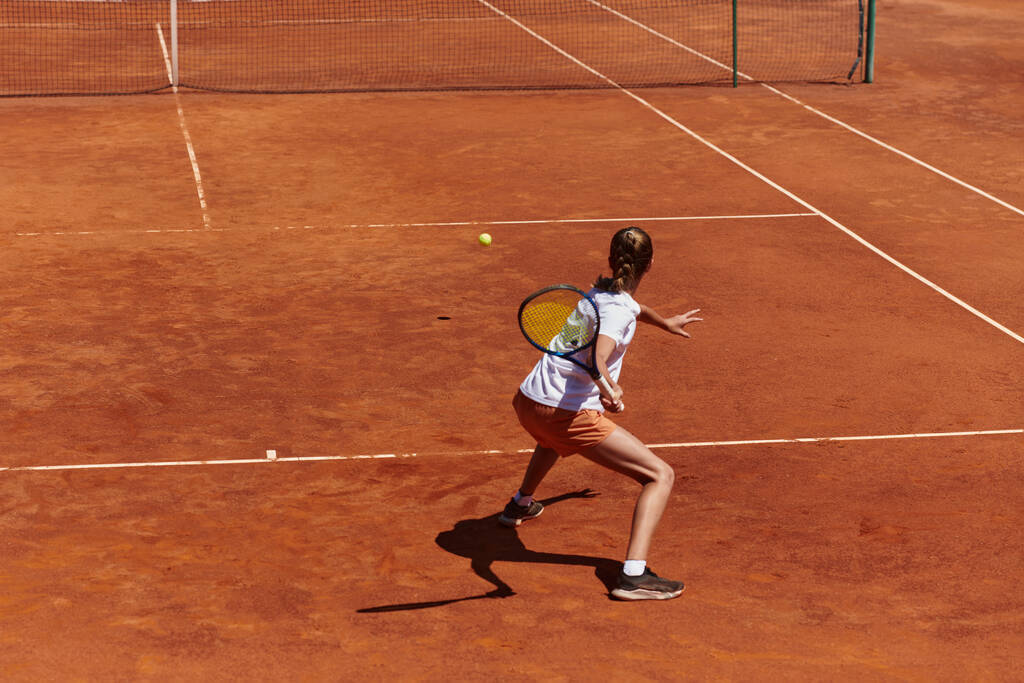 Una giovane ragazza che dimostra abilità nel tennis in una partita competitiva in una giornata di sole, circondata dall'estetica moderna di un campo da tennis - Foto, immagini