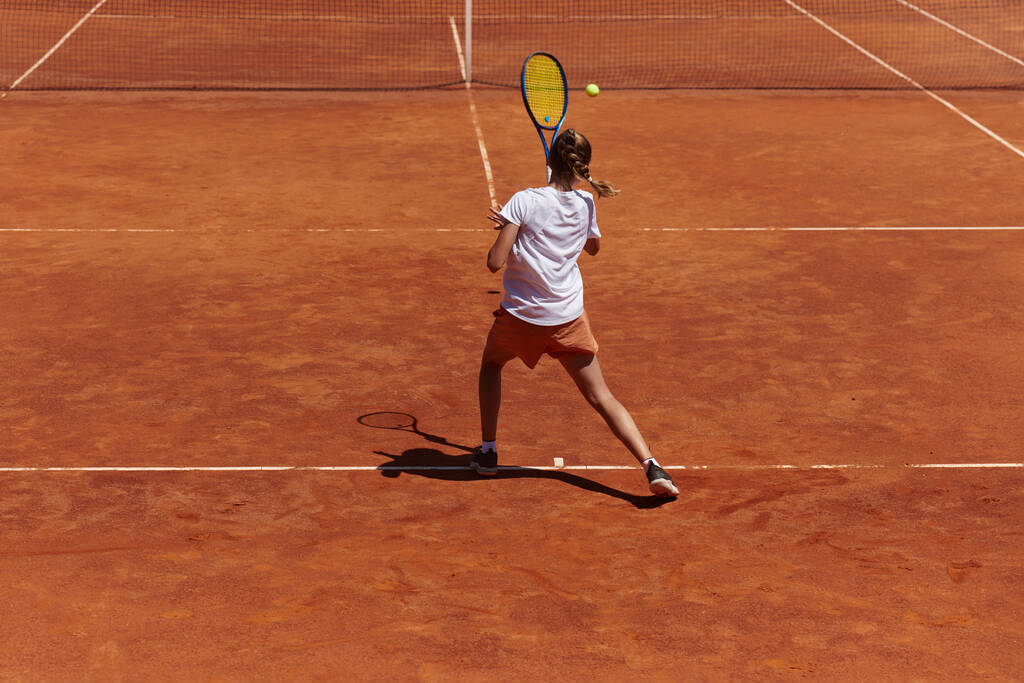 Une jeune fille montrant des compétences professionnelles de tennis dans un match de compétition par une journée ensoleillée, entouré par l'esthétique moderne d'un court de tennis - Photo, image