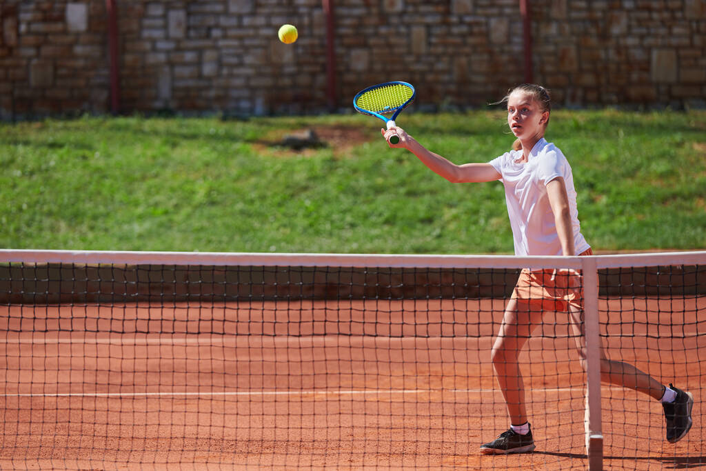 A young girl showing professional tennis skills in a competitive match on a sunny day, surrounded by the modern aesthetics of a tennis court - Photo, Image