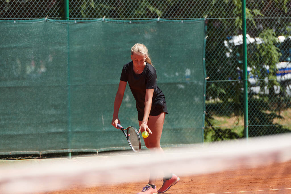 Een jong meisje met professionele tennisvaardigheden in een wedstrijd op een zonnige dag, omringd door de moderne esthetiek van een tennisbaan - Foto, afbeelding