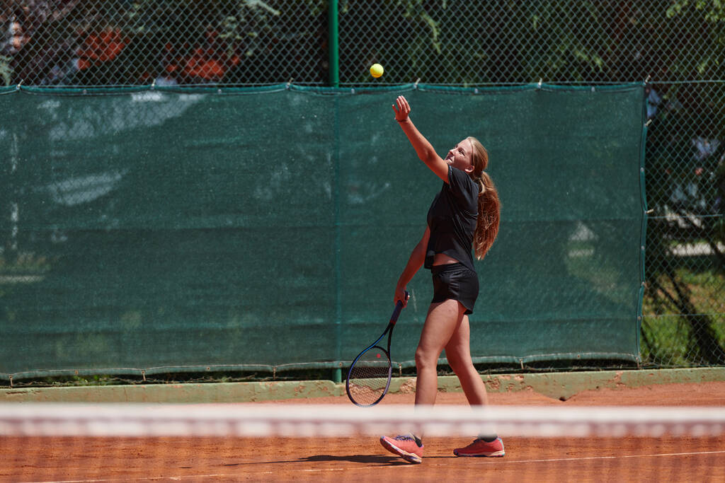 Egy fiatal lány, aki profi tenisztudást mutat egy versenymérkőzésen egy napsütéses napon, körülvéve egy teniszpálya modern esztétikájával - Fotó, kép
