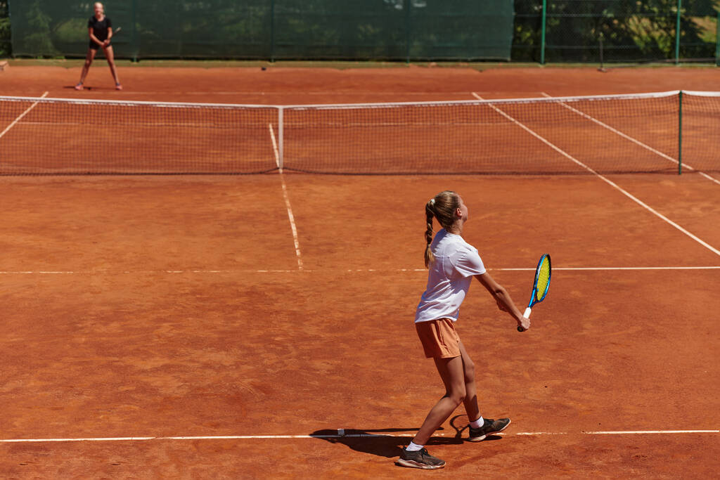 Nuoret tytöt vilkkaassa tennisottelussa aurinkoisena päivänä, osoittaen taitojaan ja innostustaan nykyaikaisella tenniskentällä. - Valokuva, kuva