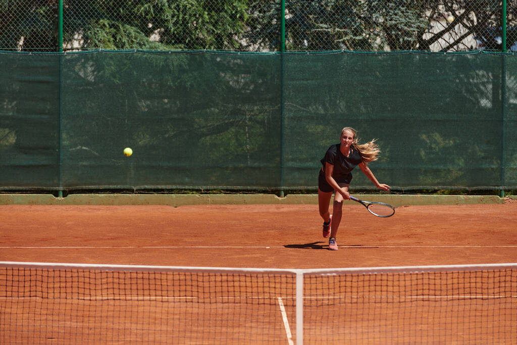 Ein junges Mädchen zeigt in einem Wettkampf an einem sonnigen Tag professionelle Tennisfähigkeiten, umgeben von der modernen Ästhetik eines Tennisplatzes - Foto, Bild