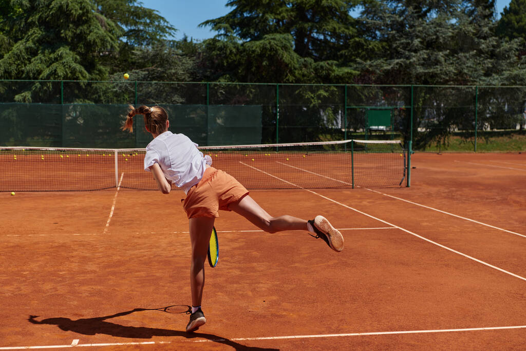 Tenis oyuncusu dikkatle odaklanarak, tenis kortuna yaptığı servisi hassasiyetle ve kararlılıkla mükemmelleştiriyor ve yeteneklerini geliştirmeye olan bağlılığını gösteriyor. - Fotoğraf, Görsel