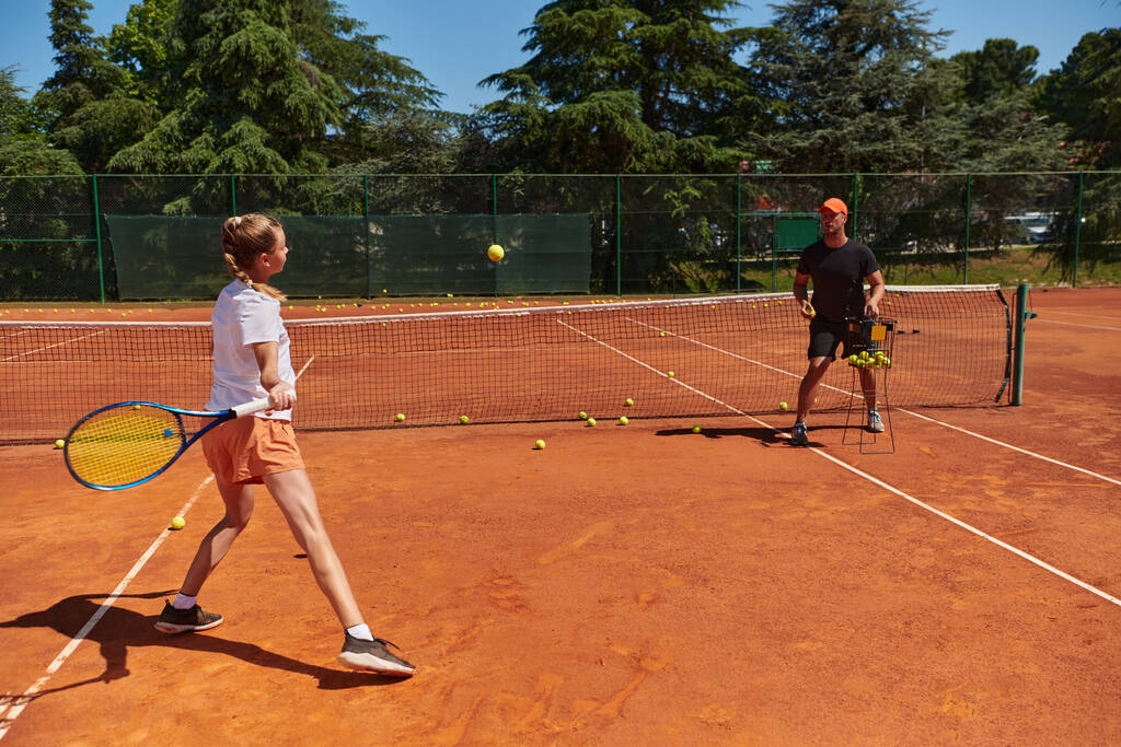 Profesyonel bir tenisçi ve onun koçu tenis kortunda güneşli bir günde antrenman yapıyorlar. Profesyonel bir tenisçinin antrenmanı ve hazırlığı. - Fotoğraf, Görsel
