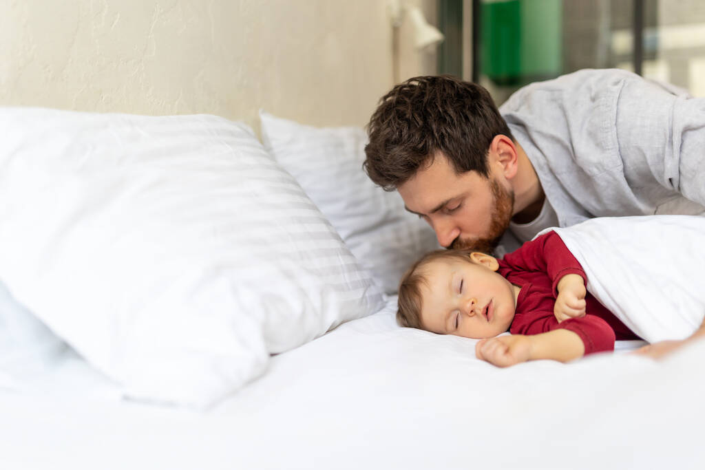 Jóképű barna apa csók alvó csecsemő baba gyengéden otthon belső. - Fotó, kép