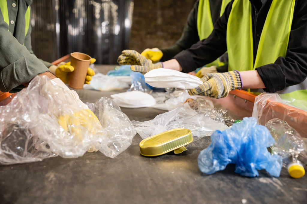 Widok pracowników w kamizelkach i rękawicach o wysokiej widoczności oddzielających różne plastikowe i papierowe śmieci na przenośnikach podczas pracy na stacji utylizacji odpadów, koncepcja recyklingu - Zdjęcie, obraz