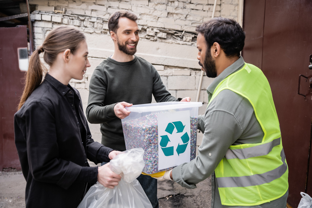 Glimlachende vrijwilligers die afval geven aan Indiase werknemers in hoogzichtvest in afvalverwerkingsstation buiten, afvalsorteer- en recyclingconcept - Foto, afbeelding