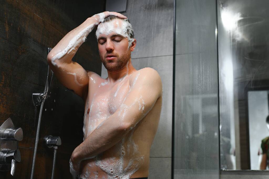 Bonito jovem tomando um chuveiro sob queda gotas de água lavando corpo nu e cabeça no banheiro moderno em casa. Modelo masculino. - Foto, Imagem