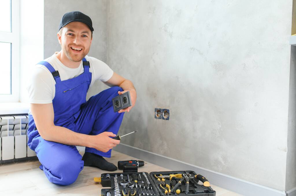 Usmívající se profesionální elektrikář v uniformě nahrazující zásuvku v bytě po rekonstrukci. - Fotografie, Obrázek