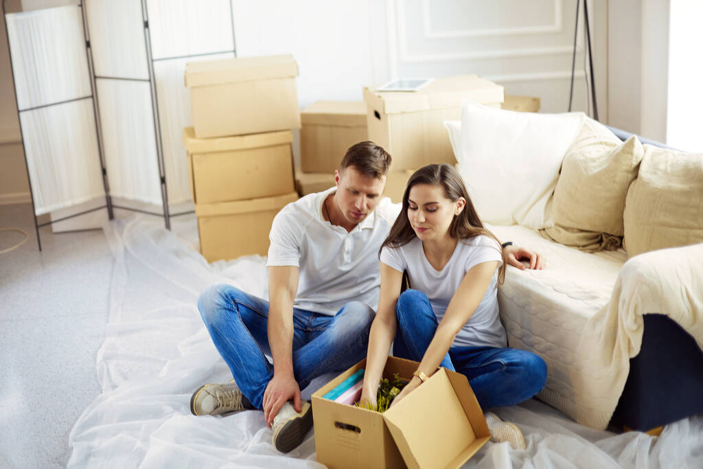 Счастливая молодая пара распаковывает коробки и переезжает в новый дом
. - Фото, изображение
