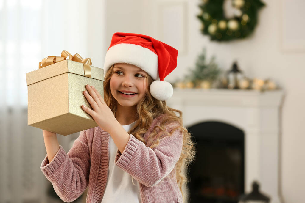 Szczęśliwa dziewczynka z prezentem świątecznym przy kominku w domu. Miejsce na tekst - Zdjęcie, obraz