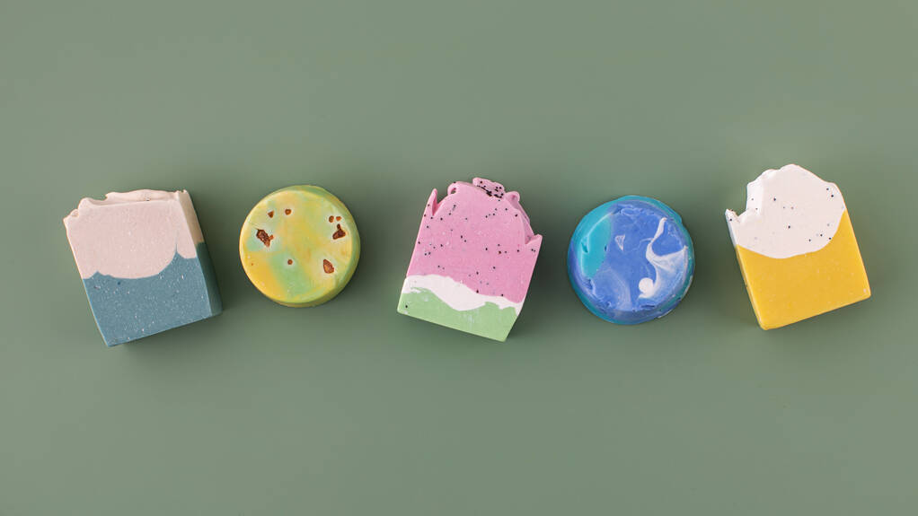 Kousky různých tvarů a barev ručně vyrobeného mýdla na zeleném pozadí. Koncept přírodní kosmetiky, hygieny. Nápis - Fotografie, Obrázek
