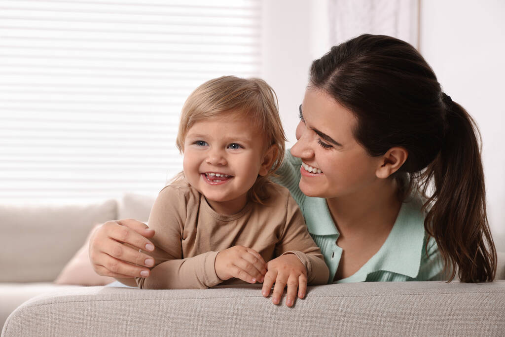 Mother with her cute little daughter on sofa at home, space for text - Foto, Bild