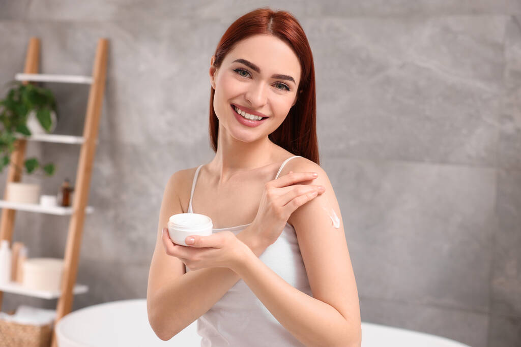 Hermosa mujer joven aplicando crema corporal en el hombro en el baño - Foto, Imagen