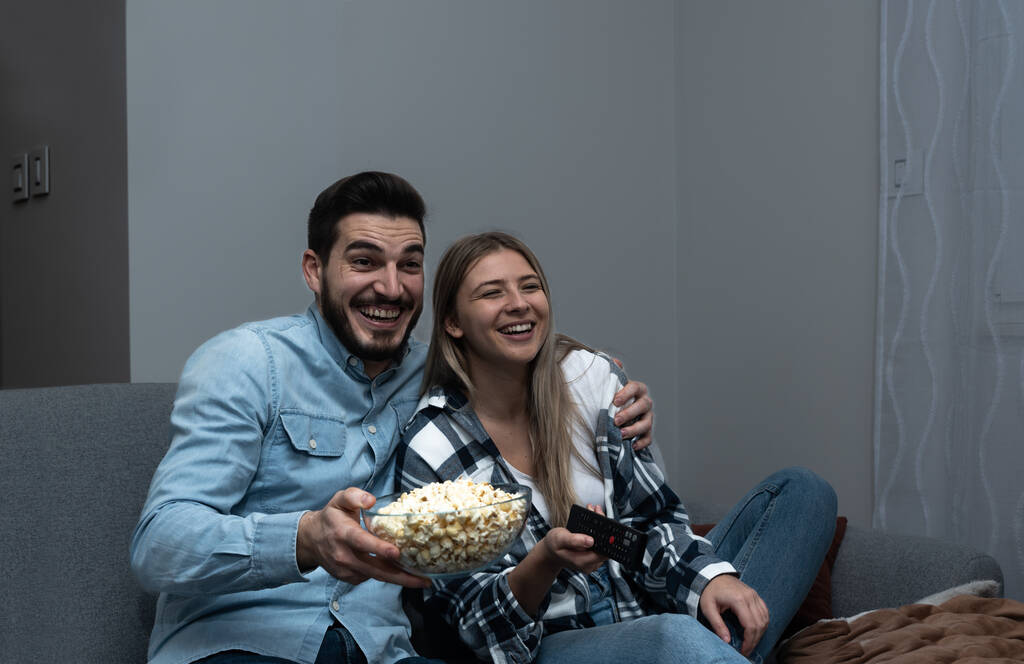 Thuis tv kijken. Loving paar rusten op de bank en het eten van popcorn terwijl u geniet van film of film op televisie - Foto, afbeelding