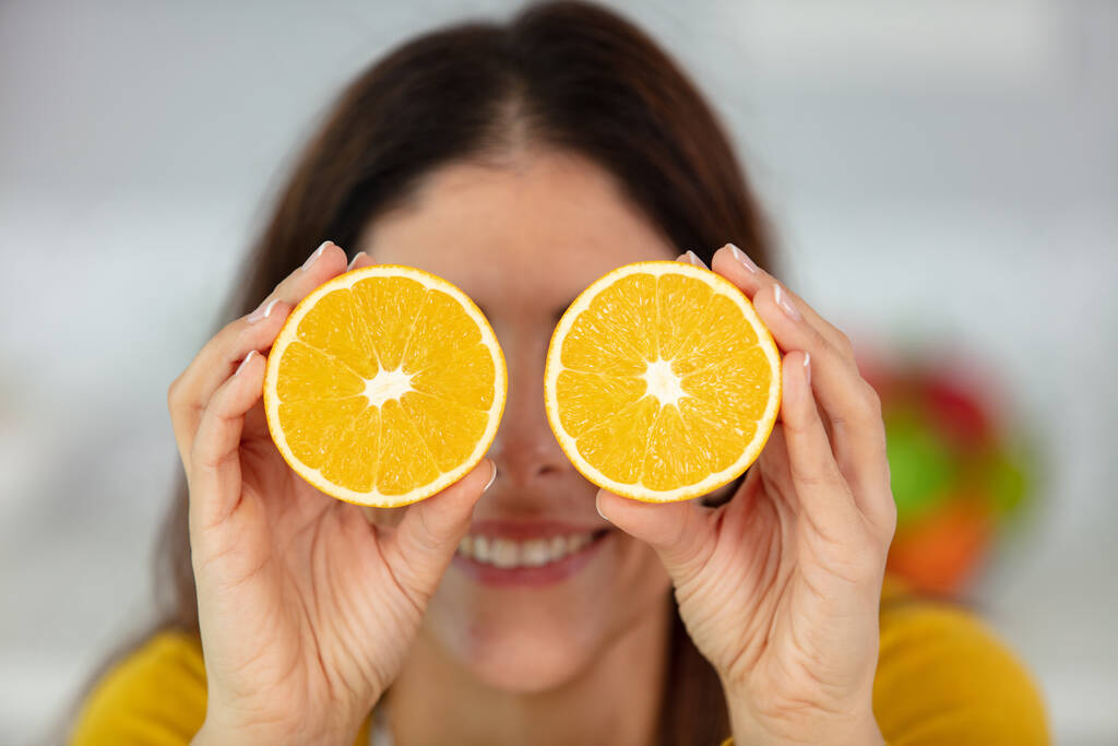 весела молода дівчина тримає помаранчеві половинки над її очима
 - Фото, зображення