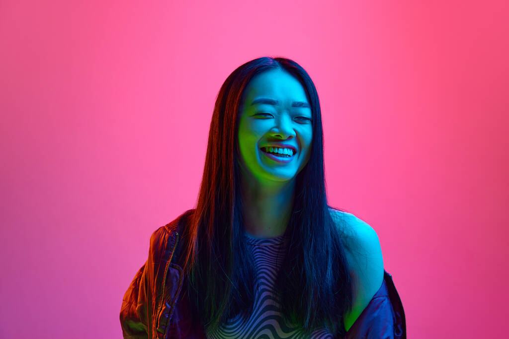 Ritratto di ragazza felice, sorridente, asiatica e giovane che posa allegramente sullo sfondo dello studio rosa in luce al neon. Felicità, successo. Concetto di emozioni, espressione facciale, gioventù, stile di vita, vendite, annuncio - Foto, immagini