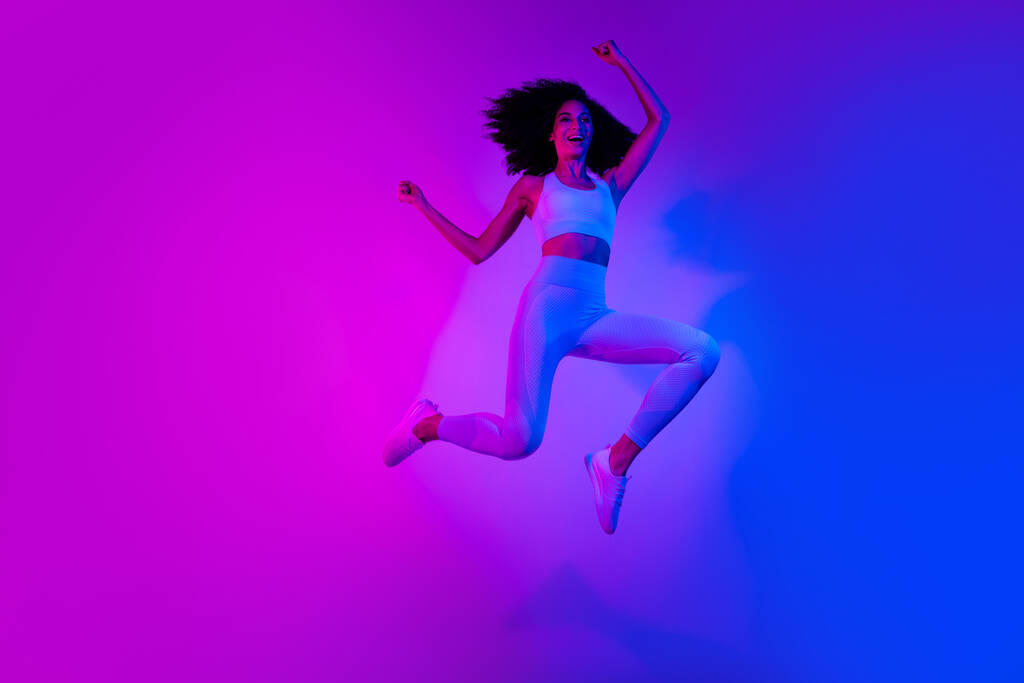 Full length photo of slim funny person jumping raise fists empty space ad leggings top shoes isolated on colorful neon background. - Photo, Image