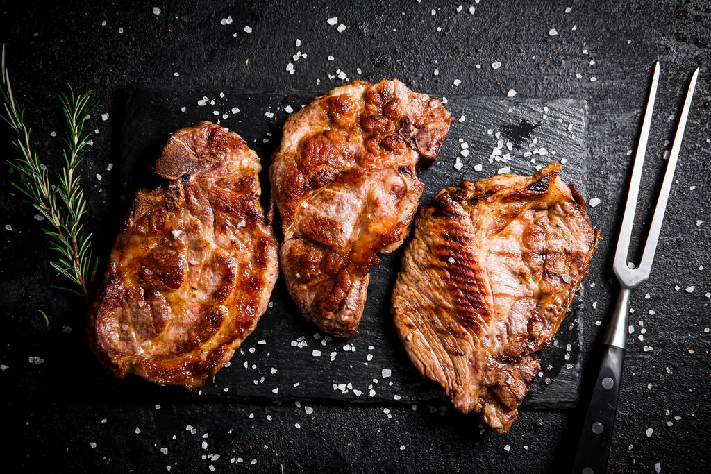 Biberiyeli ızgara domuz bifteği. Siyah bir arka planda. Yüksek kalite fotoğraf - Fotoğraf, Görsel