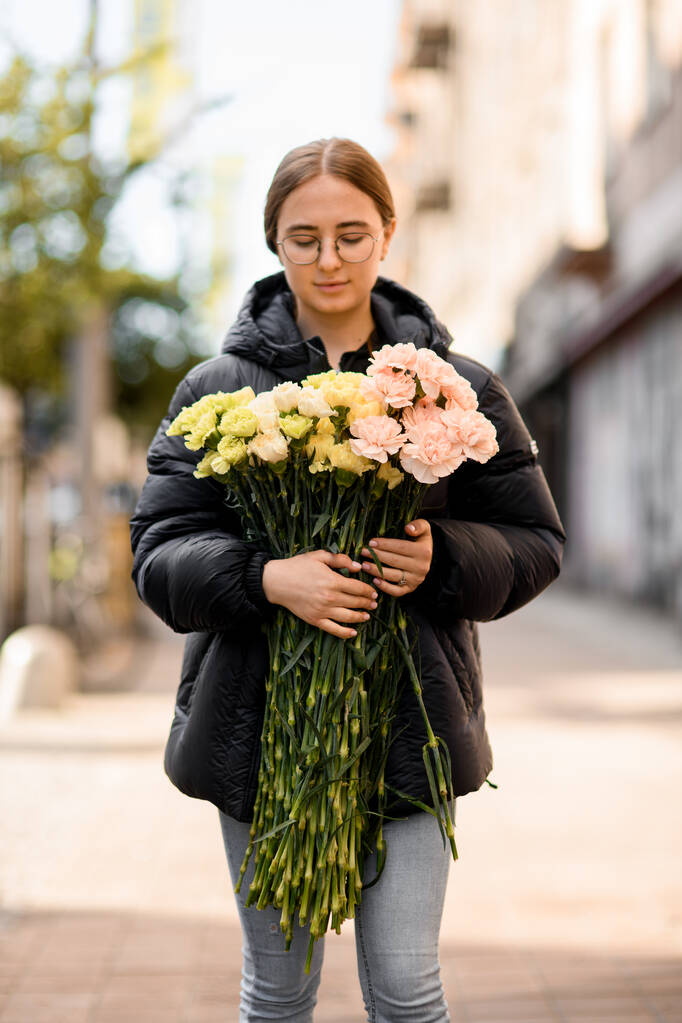 Mladá krásná žena drží v rukou velkou kytici žlutých, růžových, citrónových a mléčných karafiátů. Fotografie z ulice - Fotografie, Obrázek