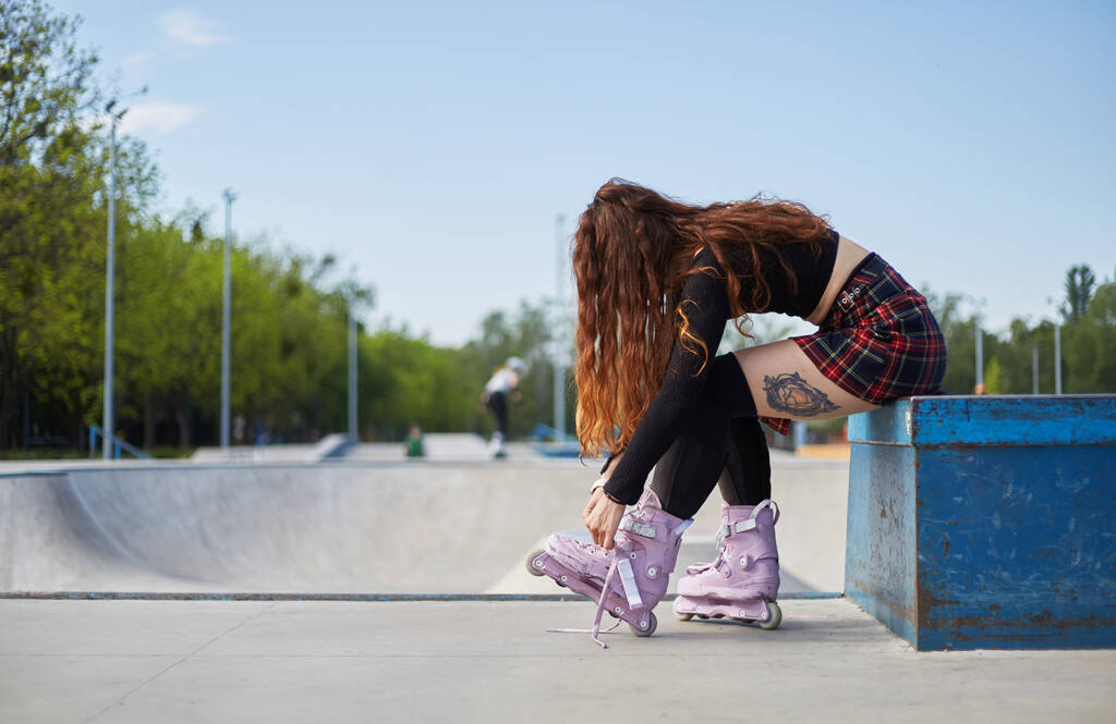 Menő, fiatal korcsolyázó nő agresszív korcsolyát vesz fel egy betondeszkás bárkába. Sportoló készül egy kört görkorcsolyával a városi parkban nyáron - Fotó, kép
