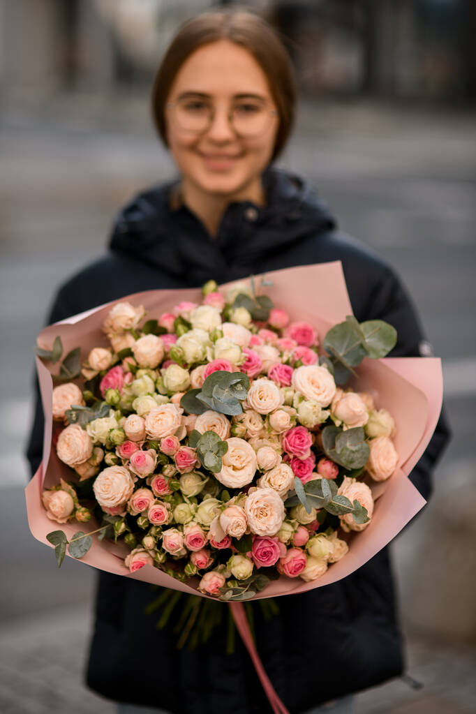 Donna fiorista tenuta in mano bel mazzo di piccole rose gentili decorate con rami di eucalipto avvolti in carta da imballaggio kraft. - Foto, immagini