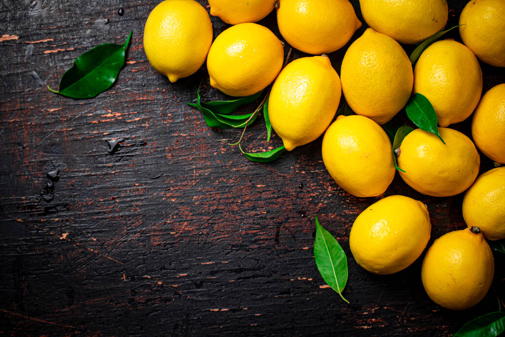 テーブルの上に葉を持つジューシーなレモン。素朴な暗い背景に。高品質の写真 - 写真・画像