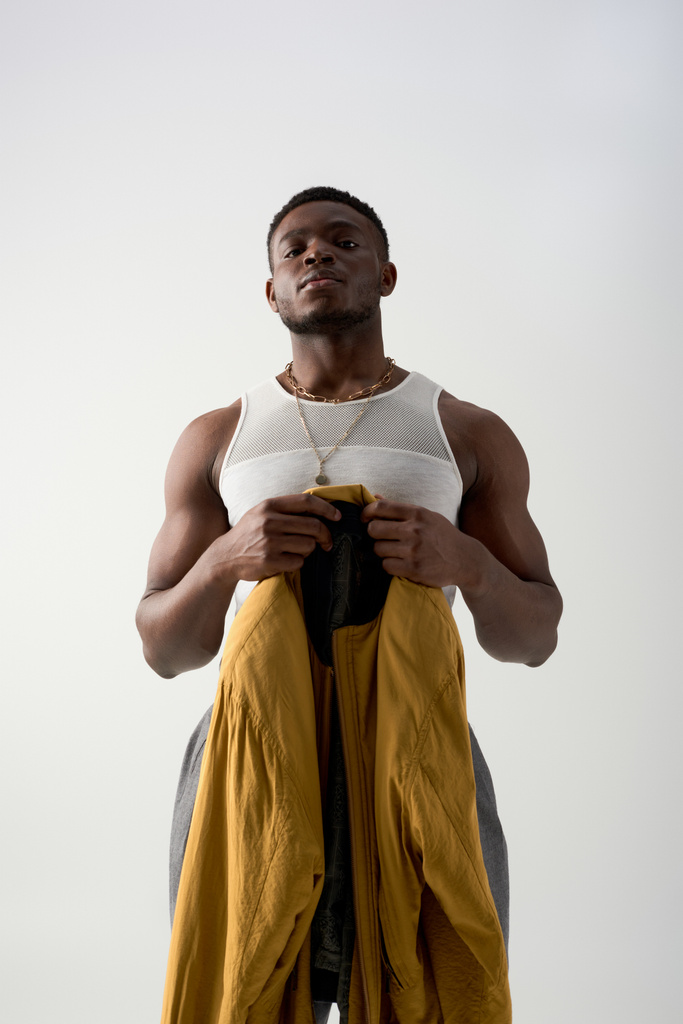 Matala kulma näkymä luottavainen nuori afrikkalainen amerikkalainen mies toppi tilalla pommikone takki eristetty harmaa, nykyaikainen ampua featuring tyylikäs puku, lihaksikas - Valokuva, kuva