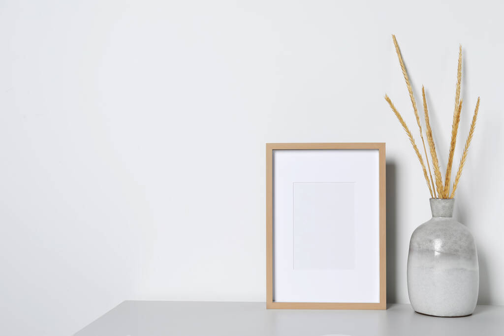 Empty photo frame and vase with dry decorative spikes on white table. Mockup for design - Photo, Image