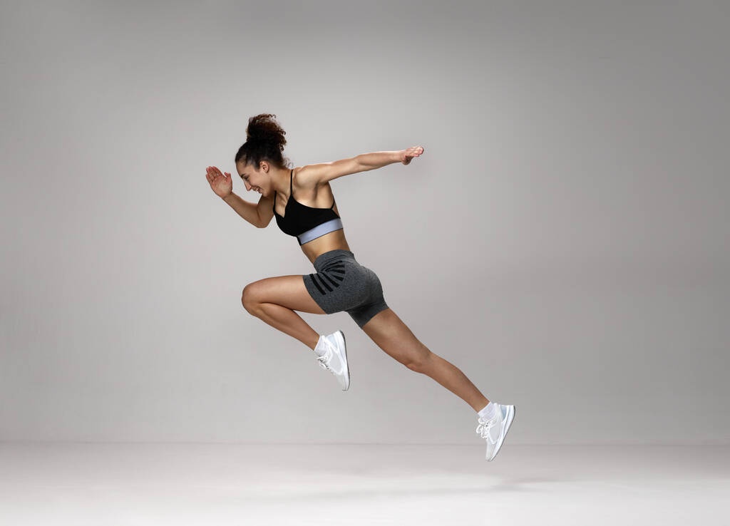 Dynamic image of sportive, young, strong woman in sportswear training, running against gray studio background. Concept of sportive lifestyle, beauty, body care, fitness, health, marathon - Photo, Image