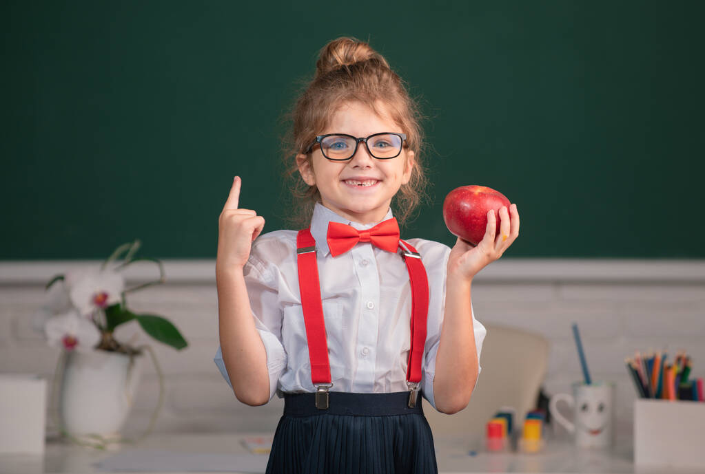 De vuelta a la escuela. Retrato de colegiala nerd estudiante mantenga manzana con sorprendente expresión apuntando con el dedo contra pizarra - Foto, Imagen