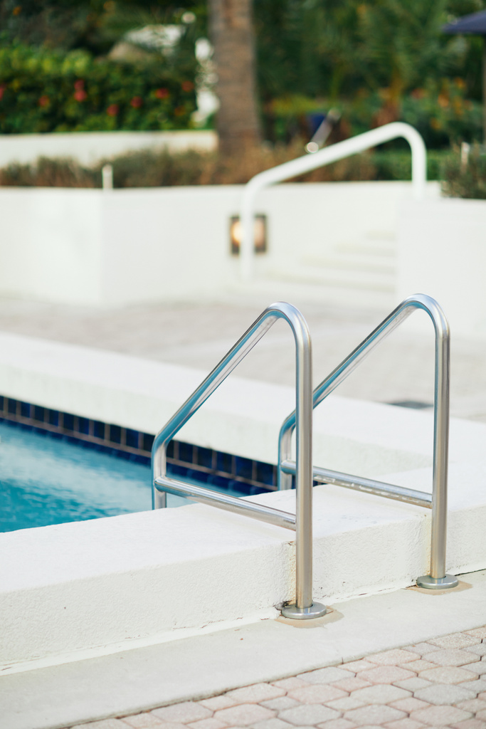 відкритий басейн з яскраво-блакитною водою та металевими сходами басейну з нержавіючою поручнями в розкішному готельному курорті, розмитим фоном, відпочинком та концепцією свята
  - Фото, зображення
