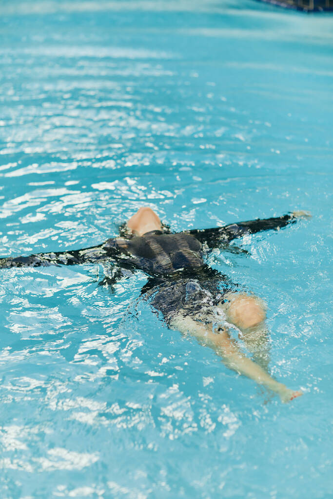 femme insouciante en vêtements noirs nageant dans l'eau bleue de la piscine extérieure dans un complexe de luxe à Miami, liberté, eau chatoyante, bonheur, liberté, détente, station balnéaire à Miami - Photo, image