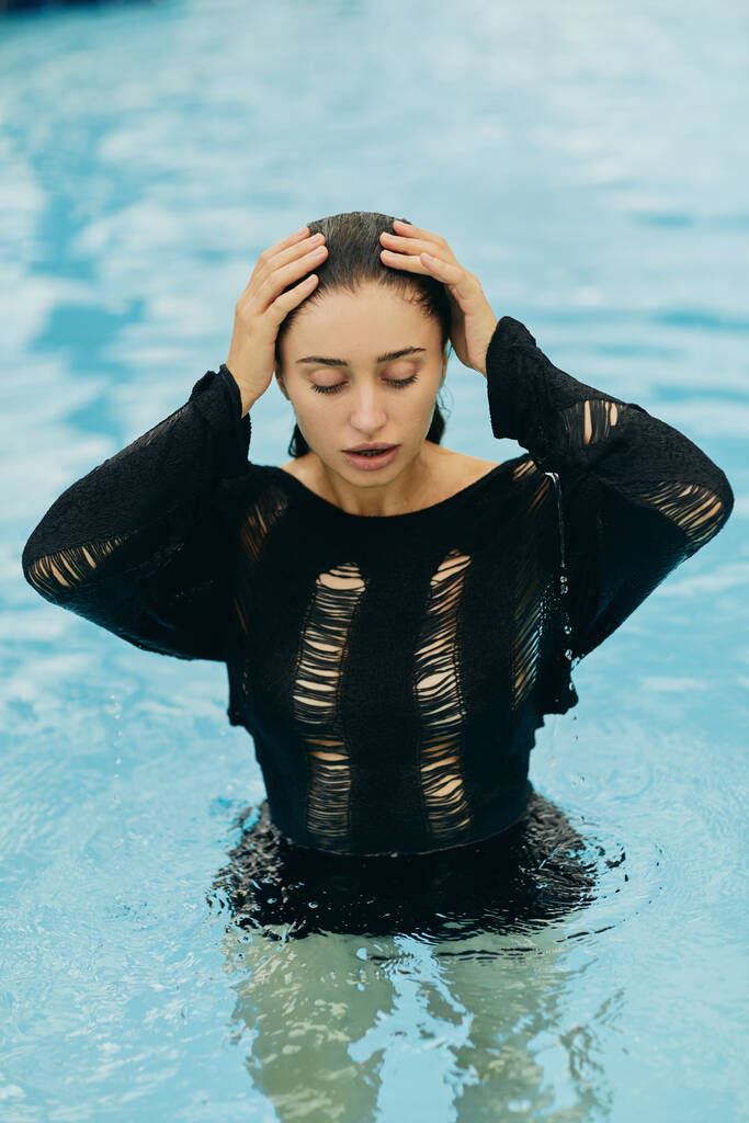 geen make-up look, mooie en sexy vrouw in zwarte gebreide outfit poseren in het buitenzwembad tijdens vakantie in Miami, verleidelijk, luxe resort, natuurlijke schoonheid  - Foto, afbeelding