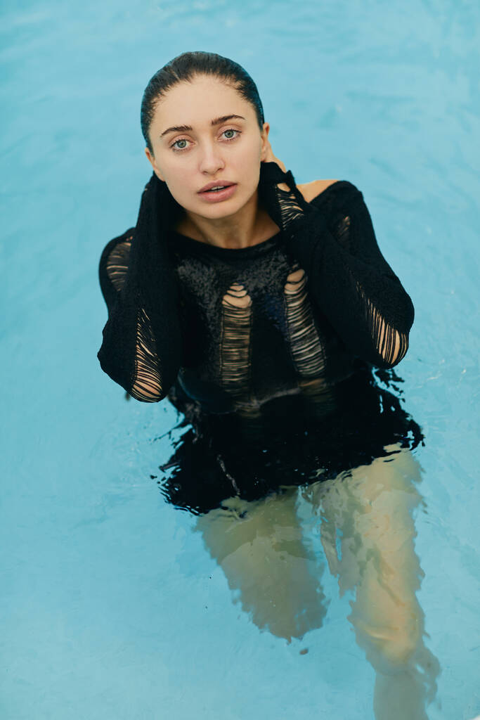 natuurlijke schoonheid, geen make-up look, natte en sexy brunette vrouw in zwart gebreide outfit poseren in het buitenzwembad tijdens vakantie in Miami, luxe resort, Florida  - Foto, afbeelding