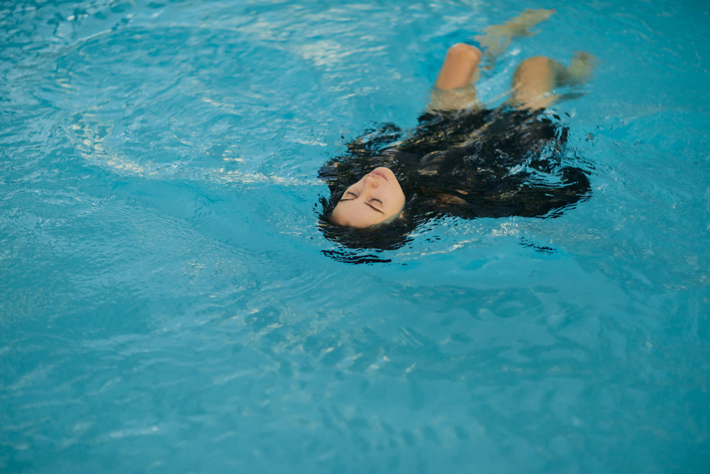 escapada de verano, mujer despreocupada en traje de baño negro nadando en agua azul de la piscina pública en el complejo de lujo en Miami, agua brillante, libertad, relajación, resort en Miami  - Foto, imagen