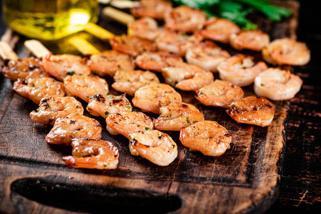 Grilled shrimp on skewers with parsley on a cutting board. Against a dark background. High quality photo - Фото, изображение