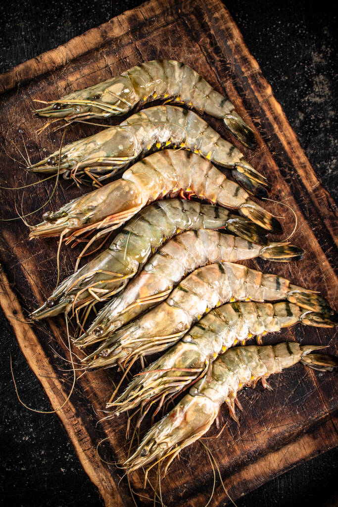 Fresh raw shrimp on a wooden cutting board. On a black background. High quality photo - Fotografie, Obrázek