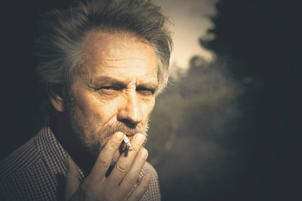 Hombre anciano fumando cigarrillos en el parque de la ciudad últimamente durante el día - Foto, imagen