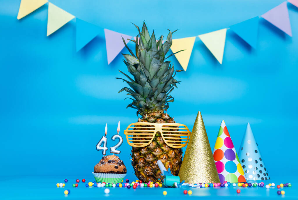 Kreatív háttér ananász karakter napszemüveg másolja a helyet. Boldog szülinapot muffinnal vagy tortával a 42-es számú gyertyával. Évforduló ünnep dekorációk egy kék háttér. - Fotó, kép