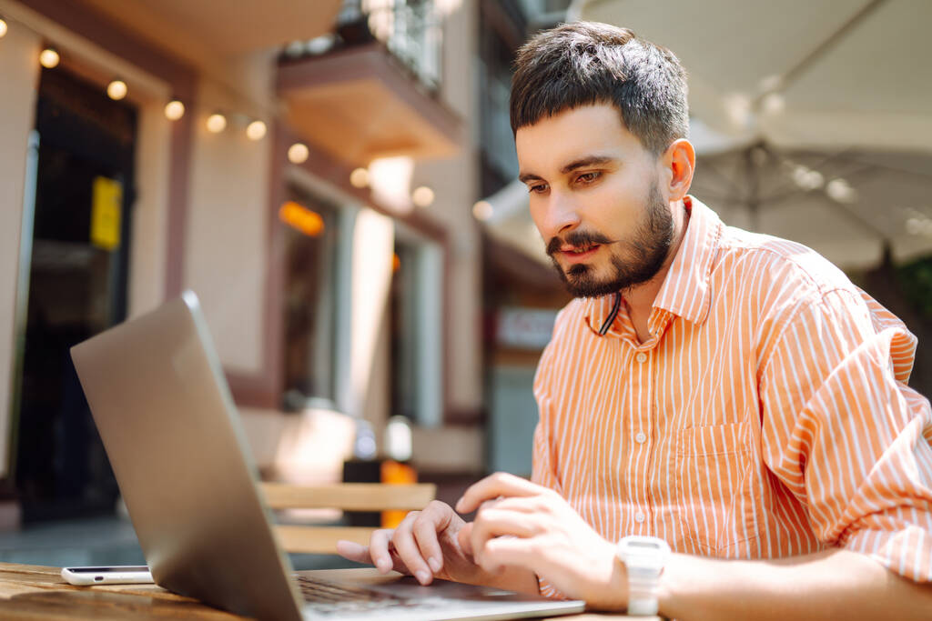 Jeune homme avec un ordinateur portable travaillant ou étudiant en ligne dans un café de rue. Concept pour l'éducation, entreprise, blog ou freelance. - Photo, image