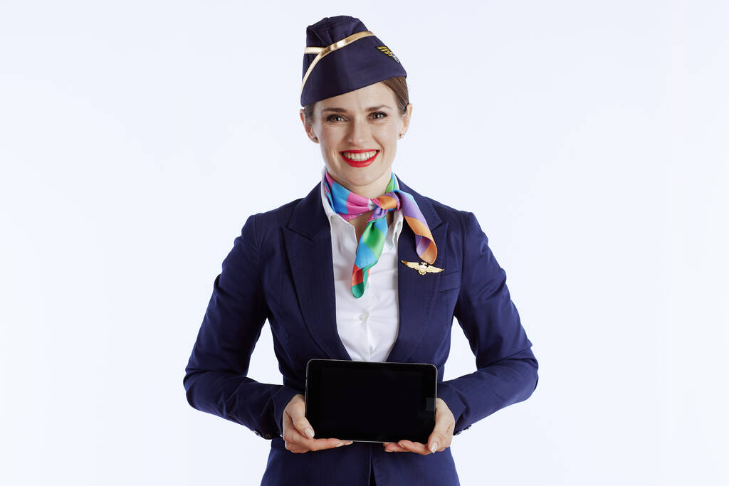 glücklich moderne Stewardess Frau vor weißem Hintergrund in Uniform zeigt Tablet-PC leeren Bildschirm. - Foto, Bild