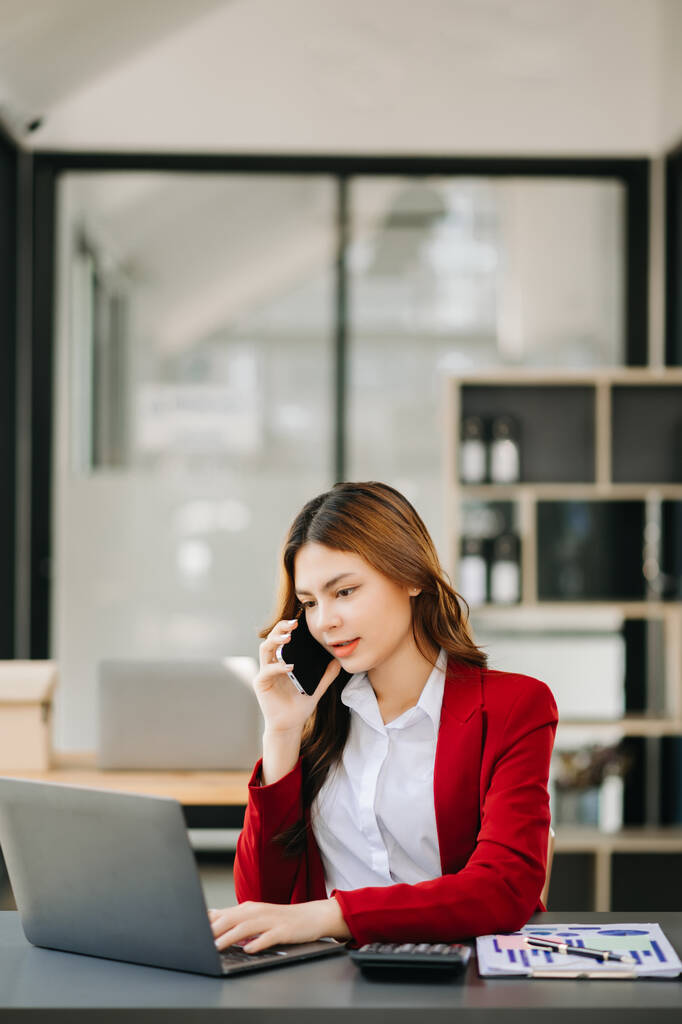 Biznes azjatycka kobieta Rozmawianie przez telefon i za pomocą laptopa z uśmiechem podczas siedzenia w biurze - Zdjęcie, obraz