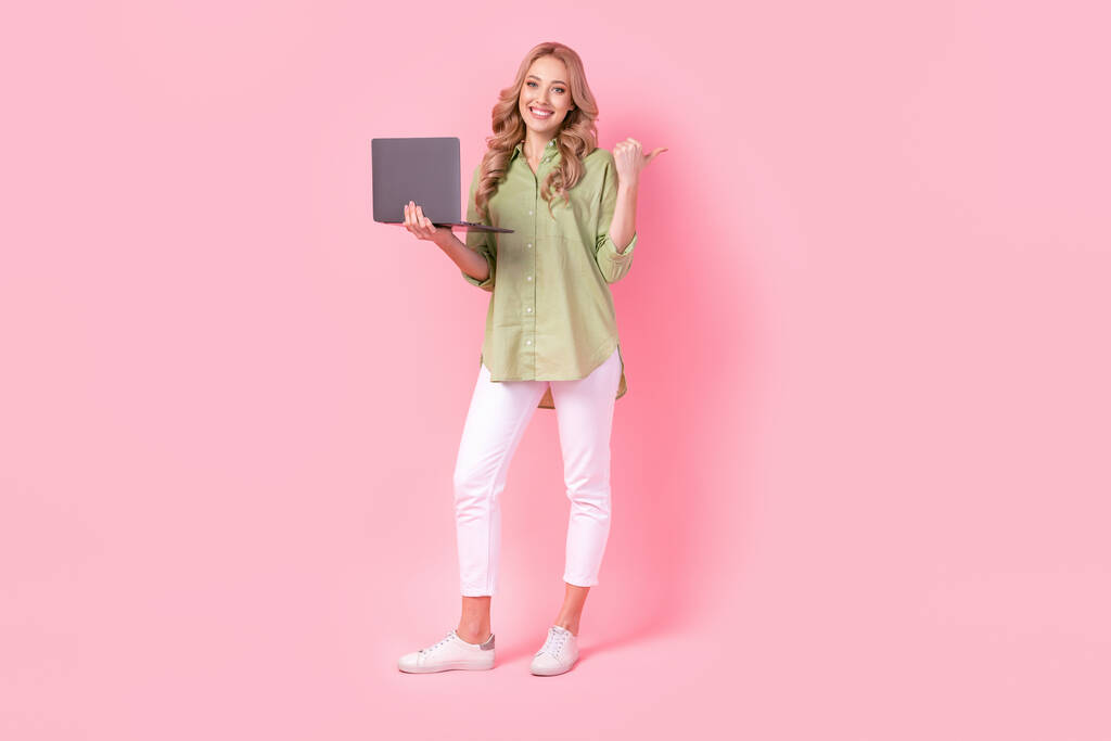 Pełna długość zdjęcie błyszczące słodkie lady nosić zieloną koszulę wpisując nowoczesne urządzenie wskazując kciuk puste miejsce odizolowane różowy kolor tło. - Zdjęcie, obraz