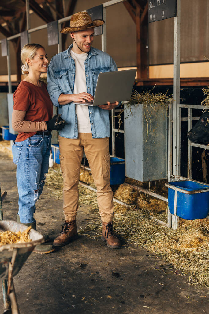 Dos jóvenes de pie en una granja de animales y haciendo inspección con el ordenador portátil. - Foto, imagen