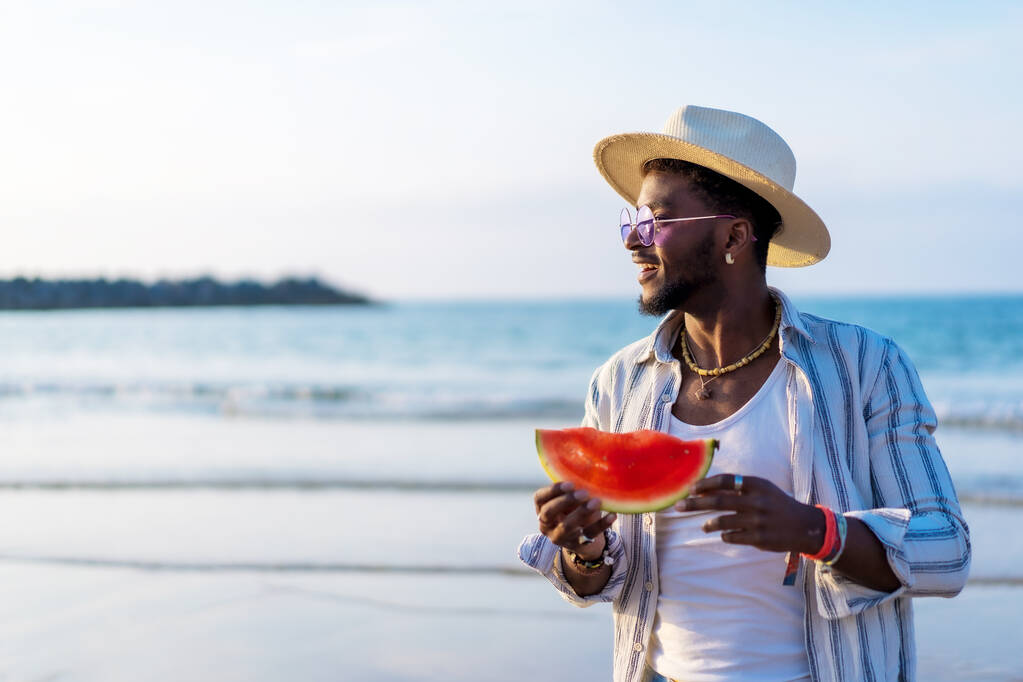Muotokuva musta etninen mies nauttia kesäloma rannalla syö vesimeloni - Valokuva, kuva